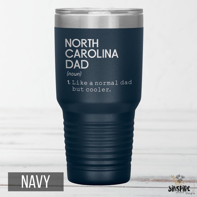 May include: Navy blue insulated tumbler with a silver lid. The tumbler features the text "NORTH CAROLINA DAD (noun) 1. Like a normal dad but cooler." The word "NAVY" is at the bottom of the tumbler.