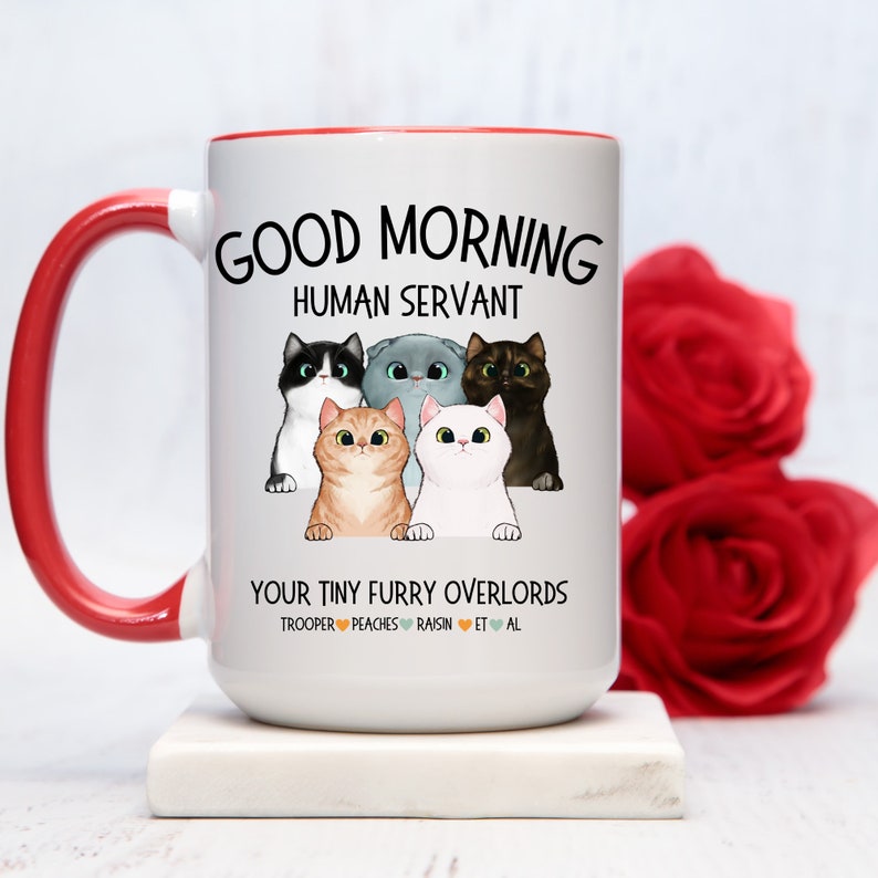 Puede incluir: Taza de caf&eacute; de cer&aacute;mica blanca con borde y asa rojos. La taza presenta una ilustraci&oacute;n de dibujos animados de cinco gatos con el texto "Good Morning Human Servant Your Tiny Furry Overlords Trooper Peaches Raisin Et Al".