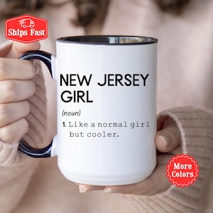 Könnte beinhalten: Ein weißer Keramikbecher mit dunkelblauem Henkel und blauem Innenrand. Auf der Vorderseite steht in schwarzer Schrift: NEW JERSEY GIRL (noun) 1. Like a normal girl but cooler. Der Becher hat einen zylindrischen Körper und einen geschwungenen Henkel.
