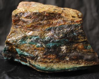 May include: A large, rough, irregularly shaped rock with layers of brown, green, and black. The rock has a natural, unpolished finish.