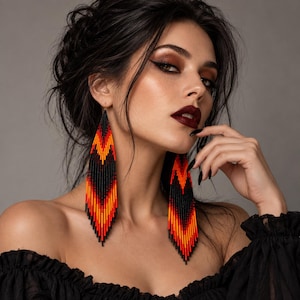 Peut inclure: Longues boucles d'oreilles pendantes triangulaires fabriquées à partir de minuscules perles de rocaille dans un motif dégradé vibrant. Le design présente des rayures en chevron alternées de noir, orange vif et rouge profond.