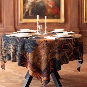 May include: A round dining table with a dark, multi-colored landscape-patterned tablecloth featuring trees and foliage. The table is set with white plates, white napkins, and two silver-toned candlesticks, positioned beneath a brass chandelier.