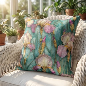 Puede incluir: Un cojín cuadrado decorativo con un diseño floral. El cojín presenta un fondo turquesa con un patrón de flores de iris en tonos de rosa, amarillo y blanco. El cojín está colocado sobre una silla de mimbre blanca.