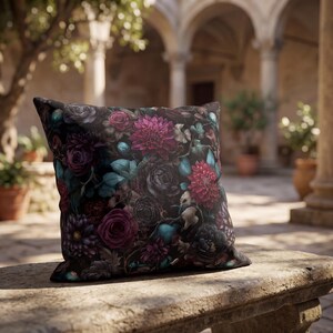 May include: A square throw pillow featuring a dark black background adorned with a dense, vibrant floral pattern. The design includes deep magenta, purple, and dark red flowers mixed with teal green leaves and foliage, creating a rich, layered botanical print.