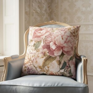 May include: A square decorative pillow with a floral pattern featuring large pink peonies and green leaves. The pillow is placed on a light blue chair with a carved wooden frame, creating a vintage aesthetic.
