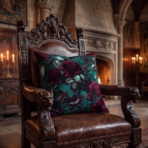 May include: A decorative throw pillow with a dark teal background and a floral pattern of burgundy roses and green leaves. The pillow rests on a brown leather armchair with ornate wooden carvings.