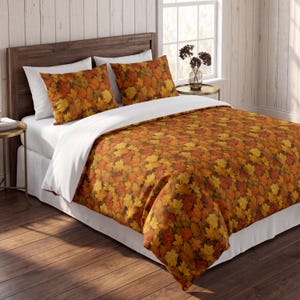 Pode incluir: Um conjunto de roupa de cama com uma capa de edredão e duas fronhas com um padrão denso de folhas de ácer de outono em tons de laranja, amarelo, vermelho e castanho. A roupa de cama é combinada com um lençol branco e fronhas brancas.