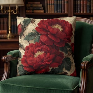 May include: A square throw pillow featuring a detailed botanical print of large, deep red peony flowers with yellow centers and dark green leaves. The background is a light beige fabric with a subtle, swirling, tone-on-tone damask pattern.