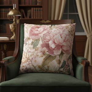 May include: A square decorative pillow with a floral pattern featuring large pink peonies and smaller white flowers. The pillow is set on a green velvet armchair with a dark wooden frame, creating a vintage aesthetic.