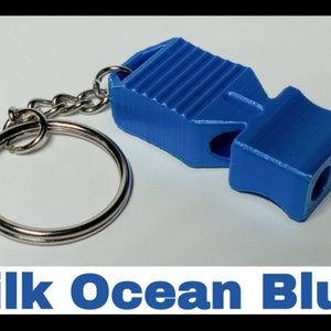 May include: A blue whistle keychain with a silver key ring. The whistle has a ribbed design and two holes for blowing. The text "Silk Ocean Blue" is printed below the image.