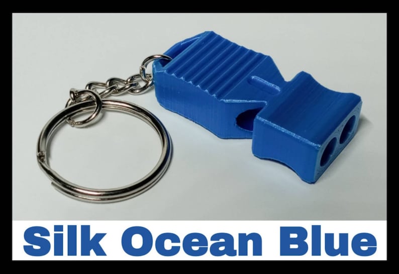 May include: A blue whistle keychain with a silver key ring. The whistle has a ribbed design and two holes for blowing. The text "Silk Ocean Blue" is printed below the image.
