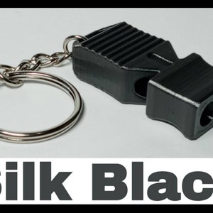 May include: A black whistle with a silver keychain. The whistle has a textured surface and two holes for blowing. The text "Silk Black" is printed below the image.