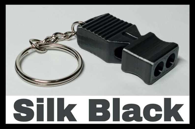 May include: A black whistle with a silver keychain. The whistle has a textured surface and two holes for blowing. The text "Silk Black" is printed below the image.