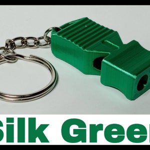 May include: A green whistle with a silver keychain. The whistle has a textured surface and two holes for blowing. The keychain is a simple silver ring.