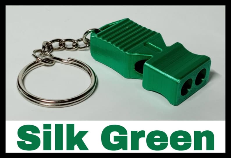 May include: A green whistle with a silver keychain. The whistle has a textured surface and two holes for blowing. The keychain is a simple silver ring.