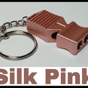 May include: A pink whistle with a silver key chain. The whistle has a ribbed design and three holes on the side.
