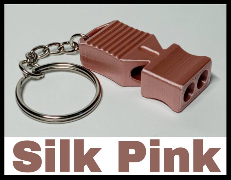 May include: A pink whistle with a silver key chain. The whistle has a ribbed design and three holes on the side.