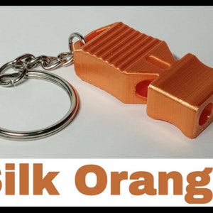 May include: A bright orange whistle with a keychain attached. The whistle has a textured surface and three holes for blowing. The text "Silk Orange" is visible below the image.