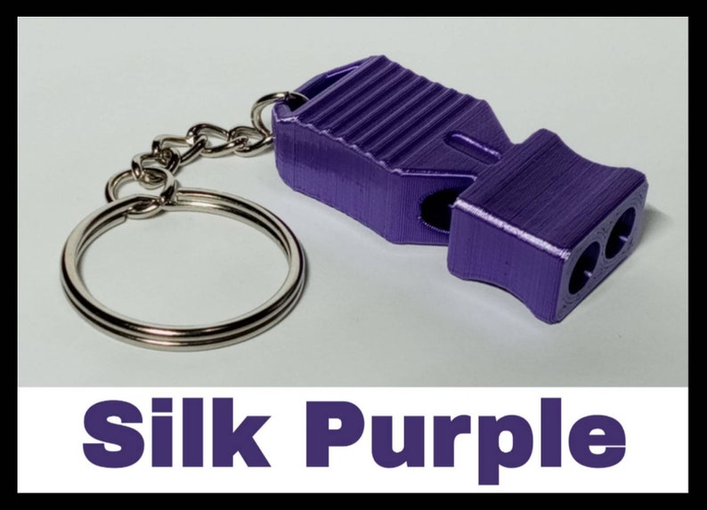 May include: A purple whistle with a silver keychain. The whistle has a textured surface and is made of metal. The keychain is a simple ring.