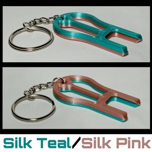 May include: Teal and pink 3D printed keychain with a key ring. The keychain is shaped like a light bulb with a small loop at the top.
