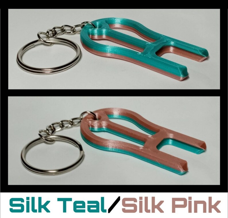 May include: Teal and pink 3D printed keychain with a key ring. The keychain is shaped like a light bulb with a small loop at the top.