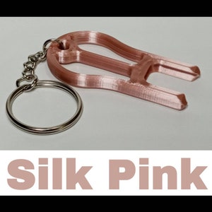May include: A rose gold-colored keychain with a loop and a small, decorative, 3D printed object attached. The object is shaped like a stylized letter "H". The text "Silk Pink" is printed below the image.