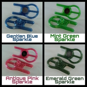 May include: Four different coloured plastic keychains with a sparkly finish. The keychains are shaped like a figure eight with a small circle in the centre. The colours are Gentian Blue Sparkle, Mint Green Sparkle, Antique Pink Sparkle, and Emerald Green Sparkle.
