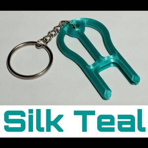 May include: Teal blue 3D printed keychain with a key ring. The keychain is shaped like a light bulb with a small loop at the top.