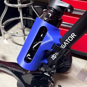 May include: A blue water bottle holder with a black water bottle inside. The holder is attached to a black bar with the text "zipN GATOR" in white. The water bottle is dark with a black lid.