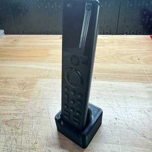 Puede incluir: Un mando a distancia negro con una pantalla y botones está sentado en una base de carga negra. El mando tiene la palabra "off" impresa en él.