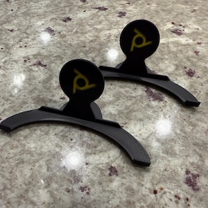 May include: Two black plastic stands with a yellow logo on the top. The stands are designed to hold something upright.