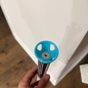 May include: A golf club putter with a blue head and a black and white striped shaft. The putter head has two circular cutouts and a circular logo. The putter is held in a person's hand.