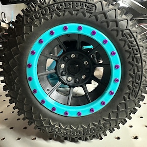 Puede incluir: Un neumático negro con una llanta azul y tuercas de rueda moradas. El neumático tiene las palabras "Go Concepts" y "SideWinder" impresas en el lateral.