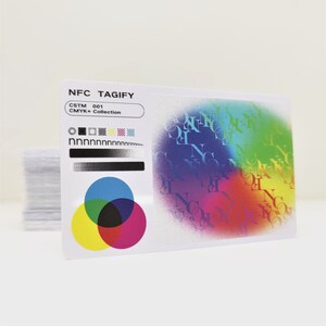 May include: A white card with the text "NFC TAGIFY" and "CSTM 001 CMYK+ Collection" printed on it. The card also features a colourful circle with the letters "NFC" printed in a rainbow pattern.