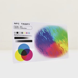 May include: A white card with the text "NFC TAGIFY" and "CSTM 001 CMYK+ Collection" printed on it. The card has a colourful design with a circle of overlapping coloured circles in the centre and a repeating pattern of the letters "NFC" in a rainbow of colours.