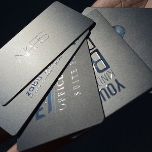 May include: A stack of five silver business cards with different text on each card. The text on the cards includes "Zabu", "Office Suite", "You Kind", and "VK6".