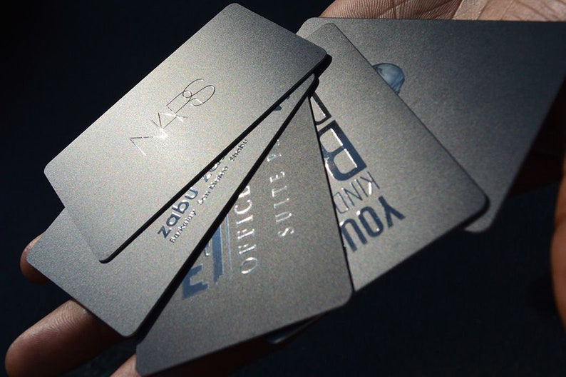 May include: A stack of five silver business cards with different text on each card. The text on the cards includes "Zabu", "Office Suite", "You Kind", and "VK6".