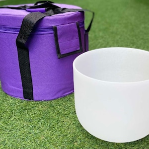 May include: A white crystal singing bowl with a purple carrying case. The bowl is made of quartz crystal and is used for sound healing and meditation.