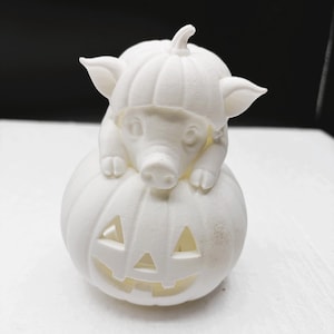 May include: A white 3D printed figurine featuring a small piglet wearing a pumpkin hat, resting on top of a larger carved jack-o'-lantern pumpkin. The entire object is monochromatic white with a matte finish and visible layer lines from the printing process.
