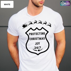 May include: White t-shirt with a black graphic featuring Santa's sleigh pulled by reindeer above a shield design. The shield reads "PROTECTING CHRISTMAS JOY 24/7". The word "WHITE" is in a white box in the upper left corner.