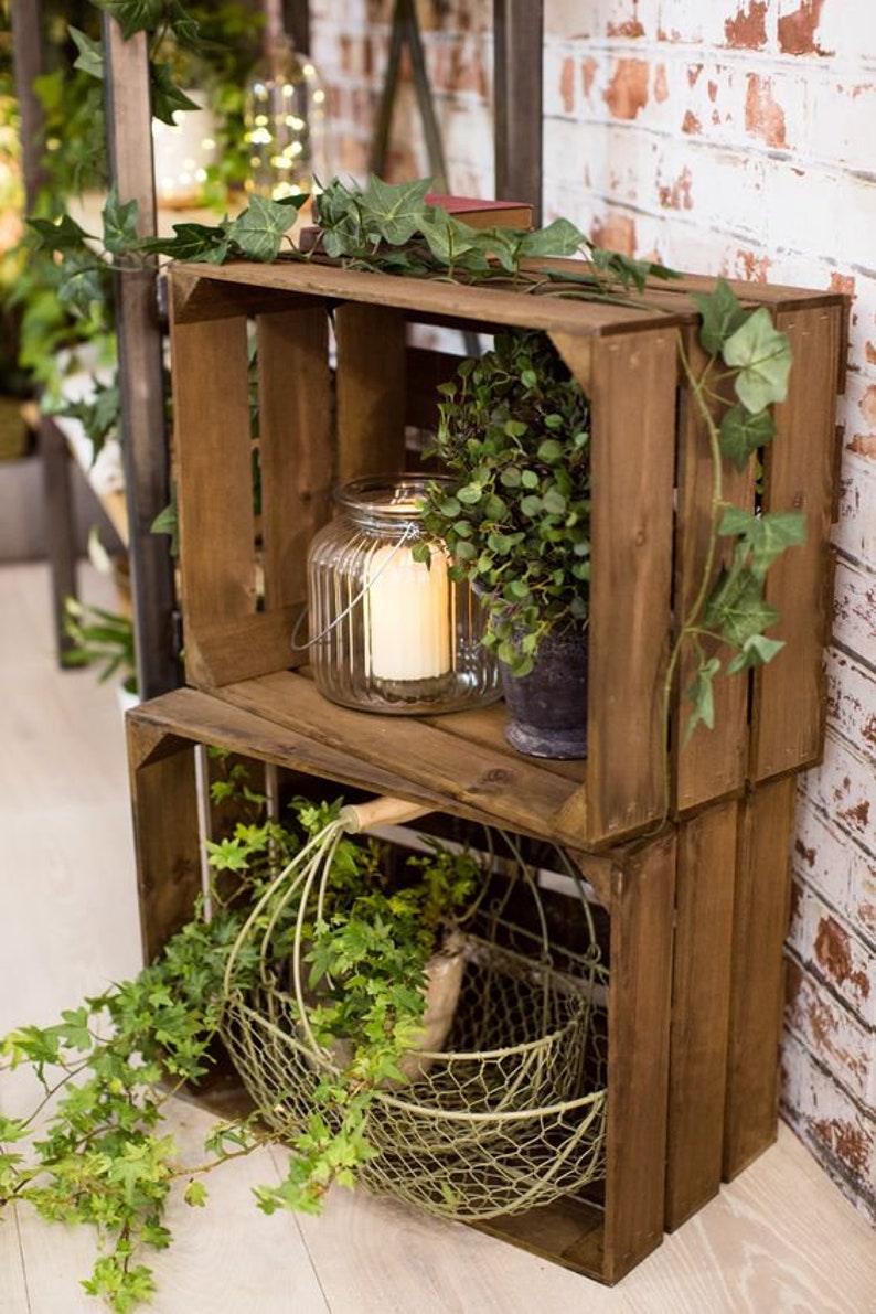 May include: Two stacked wooden crates with a wire basket and a glass candle lantern on the top shelf. The crates are decorated with green ivy vines.