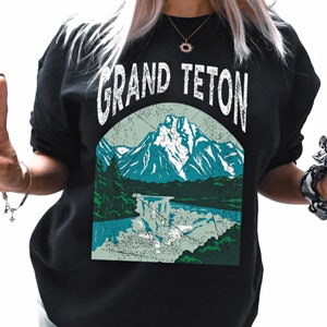 May include: Black sweatshirt with a vintage-style graphic of a mountain range and a lake. The text "GRAND TETON" is printed in white above the graphic.