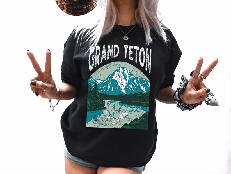 May include: Black sweatshirt with a vintage-style graphic of a mountain range and a lake. The text "GRAND TETON" is printed in white above the graphic.