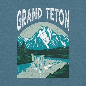 May include: A blue t-shirt featuring a graphic of the Grand Teton mountain range. The design includes a mountain with snow-capped peaks, a waterfall, and the text "GRAND TETON" in a distressed font.
