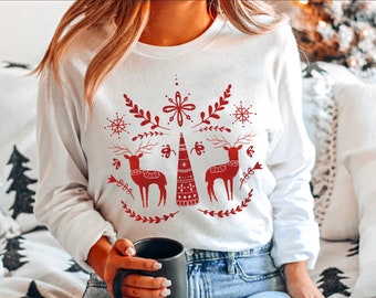 Könnte beinhalten: Weißer Langarm-Pullover mit einem roten Weihnachtsmotiv mit zwei Rentieren, einem stilisierten Weihnachtsbaum, Schneeflocken und floralen Elementen.