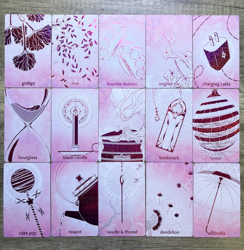 May include: A set of 16 pink and white cards with illustrations and text. Each card features a different object, such as a ginkgo leaf, rice, a knuckle duster, English ivy, a charging cable, an hourglass, a black candle, a cookpot, a bookmark, an onion, a cake pop, a teapot, a needle and thread, a dandelion, and an umbrella.