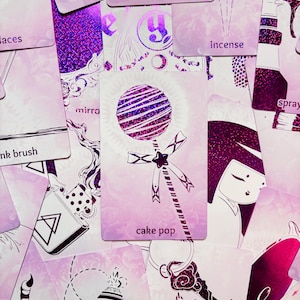 May include: A pink and purple glitter card with a white illustration of a cake pop on a stick. The card has the text "cake pop" printed on it.