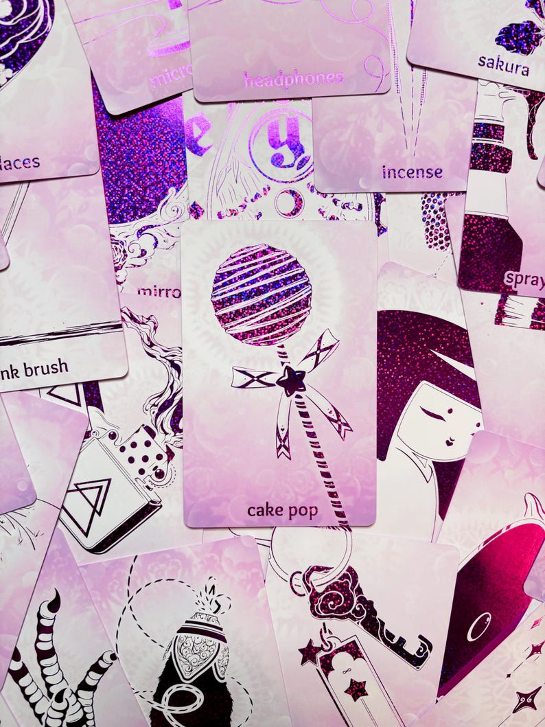 May include: A pink and purple glitter card with a white illustration of a cake pop on a stick. The card has the text "cake pop" printed on it.