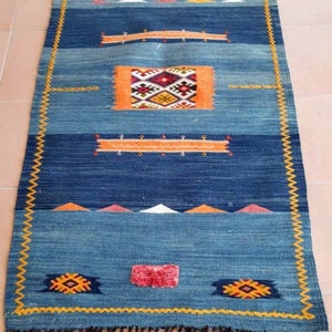May include: A blue and orange patterned rug with a fringe border. The rug has a geometric design with a central diamond shape.