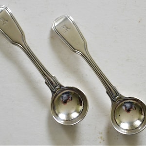 May include: Two silver teaspoons with rounded bowls and ornate handles. The handles are engraved with the letter "F".